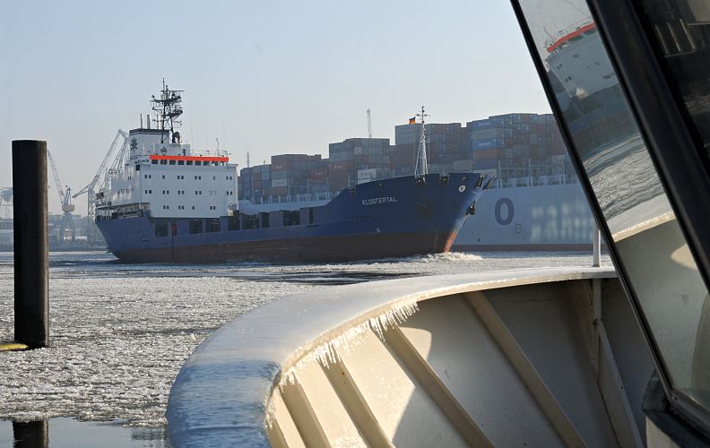 Hamburger Hafenbilder im Winter  - Eisgang auf der Elbe - Containerfeeder.  11_22733 Der niederlndische Containerfeeder Klostertal fhrt durch den Eisgang auf der Elbe flussabwrts - das Schiff spiegelt sich in der Scheibe einer Hafenfhre. Hinter dem Frachschiff luft ein hoch beladener Containerfrachter in den Hamburger Hafen ein.  www.fotograf-hamburg.de