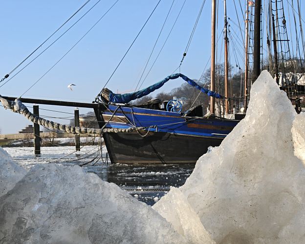 11_22737 Blick durch die Eisschollen im Museumshafen auf den Bugsprit eines historischen Segelschiffs. ©www.fotograf-hamburg.de  Bilder Hamburgs Winter - blauer Himmel, Eisschollen.