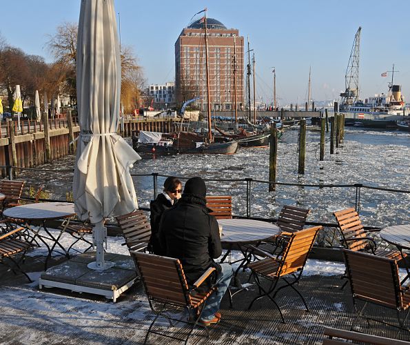 11_22738 Bei sonnigen aber frostig kaltem Hamburger Winterwetter sitzen einige Gste im Caf am Museumshafen Oevelgoenne. Im Hintergrund das ehem. Khlhaus von Hamburg Neumhlen, das jetzt als Seniorenresidenz seinen Einwohnern einen interessanten Blick ber Elbe bietet. www.fotograf-hamburg.de  Bilder vom winterlichen Hamburg, Caf Oevelgoenne