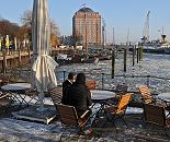 11_22738 Bei sonnigen aber frostig kaltem Hamburger Winterwetter sitzen einige Gste im Caf am Museumshafen Oevelgoenne. Im Hintergrund das ehem. Khlhaus von Hamburg Neumhlen, das jetzt als Seniorenresidenz seinen Einwohnern einen interessanten Blick ber Elbe bietet. www.fotograf-hamburg.de