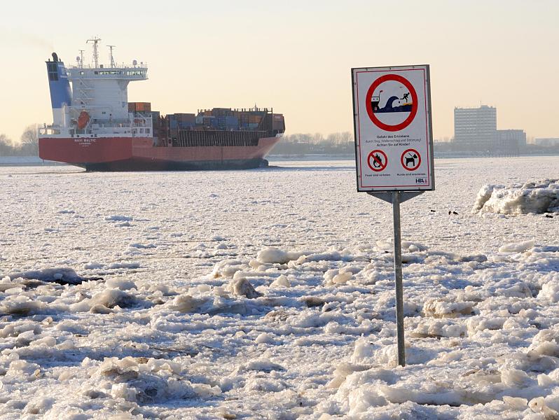 Hamburg-Fotos vom Winter - Eis auf der Elbe, Frachter. 208_5784 Zwischen dem Eis steht am Elbstrand ein Warnschild, das auf Wellenschlag und Sog sowie auf die Gefahr des Ertrinkens hinweist. Der Container Feeder NAVI BALTIC hat den Hamburger Hafen verlassen und fährt elbabwärts durch das Treibeis. 