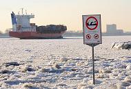 208_5784 Zwischen dem Eis steht am Elbstrand ein Warnschild, das auf Wellenschlag und Sog sowie auf die Gefahr des Ertrinkens hinweist. Der Container Feeder NAVI BALTIC hat den Hamburger Hafen verlassen und fährt elbabwärts durch das Treibeis. 