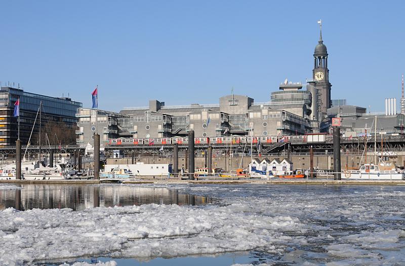 Bilder von Hamburg im Winter - blauer Winterhimmel am Niederhafen. 215_5628 Blick ber den eisbedeckten Niederhafen und Sportboothafen am Baumwall Richtung St. Michaeliskirche, eine der fnf Hauptkirchen Hamburg. Das Hamburger Wahrzeichen wird im Volksmund liebevoll " Michel" genannt. Vor dem Verlagsgebude der Gruner + Jahr AG fhrt ein Hochbahnzug zur Haltestelle Baumwall.