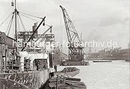 219_6_533 Vereister Grasbrookhafen - ein Ewerfhrer stakt seine Schute quer durch das dichte Eis im Hafenbecken. Frachter liegen an der Kaimauer des Dalmannkai, ihre Ladung wird gelscht oder neue Ware an Bord geladen. Ein Schwimmkran liegt lngsseits eines Frachters, er hat eine lange Holzkiste am Haken.