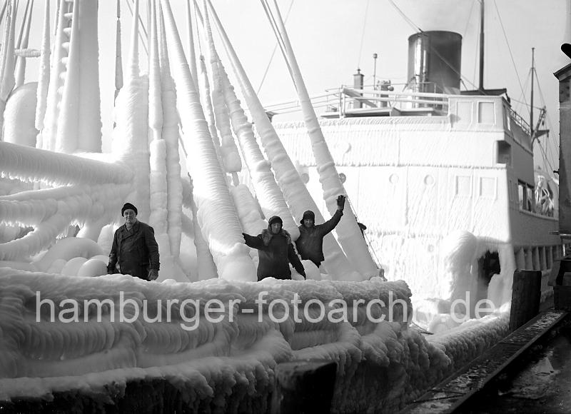 219_8_83 Die Mannschaft eines norwegischen Frachters, der garade im Hambuger Hafen eingetroffen ist, steht an Deck des stark mit Eis bedeckten Schiffs. Die Decksaufbauten und Takelage des Frachtschiffs sind mit einer sehr dicken Eisschicht überzogen.  Winter im Hamburger Hafen - vereister Frachter; Eisschicht an Deck + Takelage; ca. 1934.