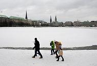 228_4983 Eine Familie mit Kindern geht mit Mtzen und Schals warm angezogen an einem grauen Wintertag an der zugefrorenen Binnenalster spazieren. Im Hintergrund der Rathausturm und die Kirchtrme von St. Petrie, St. Nikolai und der St. Michaeliskirche. 