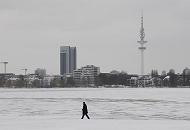 231_4981 An einem grauen Wintertag geht ein einsamer Spaziergnger am Alsterufer der zugefrorenen Alster spazieren. Am anderen Ufer des 164 ha grossen Hamburger Binnensees ragt der Fernsehturm / Heinrich Hertz Turm / Telemichel und das Radisson Hotel in den wolkenverhangenen Winterhimmel.