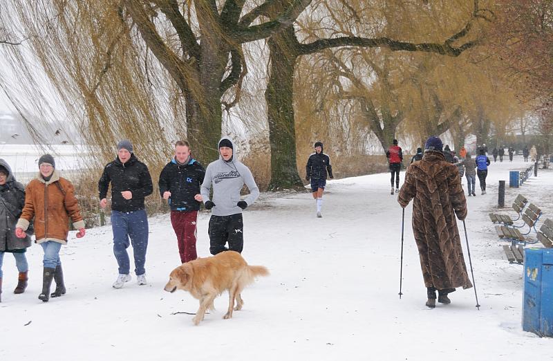 Sonntagsspaziergang an der Alster im Winter; Schneeteiben. 232_5101 Es gehrt mit zur hanseatischen Tradition am Sonntag Nachmittag einen Alsterspaziergang zu unternehmen. Eine Dame im Pelzmantel und Nordic Walking Stcke geht ihren Weg durch den Schnee am Alsterufer. Andere joggen mit kurzer Hose durch das Schneetreiben.  