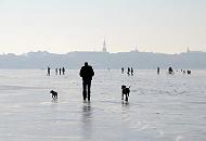 233_5484 Obwohl die zugefrorene Alster noch nicht offiziell zum Betreten freigeben ist, gehen die Hamburger auf dem Alstereis spazieren und geniessen den aussergewhnlichen Ausblick. Sie fahren sogar Fahrrad oder nehmen Ihre Hunde mit aufs Eis. Im Hintergrund der Kirchturm der  Hl. Dreieinigkeitskirche in Hamburg - St. Georg.