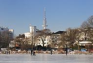 234_5514 Strahlend blauer Himmel ber dem winterlichen Hamburg - die Aussenalster ist zugefroren; Hamburger und Hamburgerinnen nutzen das schne Winterwetter und gehen mit Kinderwagen auf dem Alstereis spazieren. Andere laufen Schlittschuh auf Hamburgs grossem Binnensee. Im Hintergrund historische Hamburger Architektur an der Strasse ALSTERUFER und der Fernsehturm, der zwar den offiziellen Namen Heinrich Hertz Turm hat, aber zumeist Telemichel genannt wird.