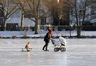 235_5468 Eine junge Mutter fhrt Schlittschuh auf dem Eis der Alster - sie schiebt dabei einen Kinderwagen und zieht einen Schlitten, auf dem ein Kind sitzt und die Winterfreuden in der Sonne geniesst.