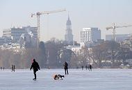 237_5509 Ein sonniger Winternachmittag in Hamburg - Spaziergänger genießen das schöne Winterwetter und gehen auf der zugefrorenen Alster spazieren. Eine Mutter läuft auf dem Eis der Alster Schlittschuh und zieht dabei ihr Kinde auf einem Schlitten. Im Hintergrund der Turm der St. Michaeliskirche.