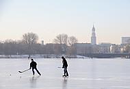 241_5574 Jugendliche spielen Eishockey auf der zugefrorenen Alster - hinter der Kennedybrücke sind die Häuser am Jungfernstieg zu erkennen und der Kirchturm der St. Michaeliskirche.