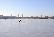 242_5558 Ein Eishockeyspieler dreht einsam seine Kurven auf dem Alstereis. Im Hintergrund das Panorama von Hamburg mit den Türmen der Hansestadt.