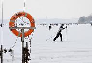 244_6093 Vor dem Anleger des Bootssteg vom Alstercafé Bobby Reich läuft ein Hamburger Ski auf der zugefrorenen und verschneiten Alster; ein verschneiter Rettungsring hängt am Steg in seiner Halterung.