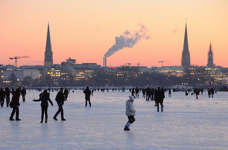 Abend an der zugefrorenen Alster - Sonnenuntergang Hamburg Panorama. 253_5950 Bis spt in den Abend geniessen die Hamburger die winterliche Atmosphre auf der zugefrorenen Alster - die untergehende Sonne frbt den Hamburger Himmel rot; aus den Schornsteinen des Heizkraftwerks in der Hafencity steigt weisser Rauch. Links der Turm der St. Jacobikirche, rechts die St. Petrikirche und die eingerstete St. Katharinenkirche. 