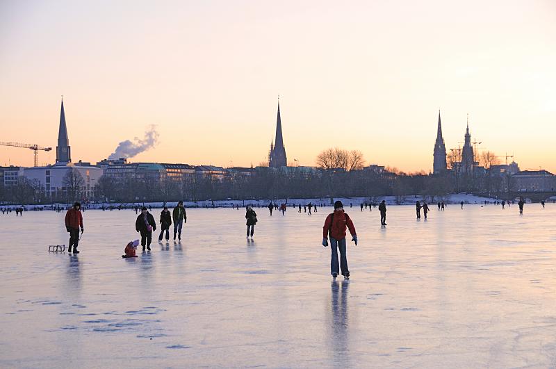 Alstervergngen auf dem Eis der Hamburger Auenalster. Hamburg Panorama mit Kirchtuermen. Bilder von Hamburg.  255_5906 Vor dem Hamburg-Panorama mit den Kirchtrmen berqueren die Hamburger auf dem Eis der Aussenalster den 156 ha grossen Hamburger Binnensee. Offiziell wird die Alster erst von der Behrde freigegeben, wenn das Eis eine Strke von 20cm hat, aber viele Hamburger laufen schon vorher z.B. mit Schlittschuhen oder Schlitten ber das Eis. 