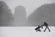 261_5054 Der Schnee fllt in dichten Flocken im Stadtpark von Hamburg Winterhude - ein junger Vater schiebt die Karre mit seinem Kind ber den schneebedeckten Fuweg auf der groen Stadtparkwiese. Im Hintergrund das Gebude des Planetariums. Der aus Ziegelsteinen errichtete Bau wurde 1915 nach einem Entwurf des Architekten Otto Menzel als Wasserturm errichtet, der 1930 dann zum Planetarium umgebaut wurde. 