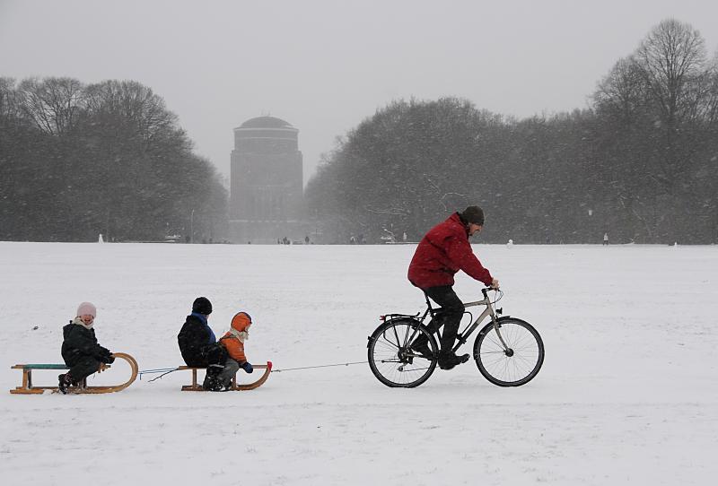 Schnee in Hamburg - Winterfreuden im Winterhuder Stadtpark. Schlittenfahren mit Fahrrad; Hamburger Planetarium.  262_5054 Der Schnee fllt in dichten Flocken im Stadtpark von Hamburg Winterhude - die groe Wiese im Zentrum des Stadtparks ist mit Schnee bedeckt. Ein Vater zieht mit seinem Fahrrad die zwei Schlitten seiner Kinder durch den Schnee.  Im Hintergrund das Gebude des Hamburger Planetariums. Der ehemalige Wasserturm wurde 1915 nach einem Entwurf des Architekten Otto Menzel errichtet, seit 1930 wird das Gebude als Planetarium genutzt.