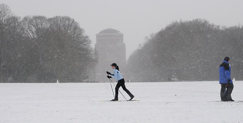 Schnee in Hamburg - Skilanglauf im Winterhuder Stadtpark.Planetarium Hamburg. 263_5059 Die groe Wiese im Zentrum des Stadtparks ist zugeschneit. Eine Skilangluferin fhrt durch den winterlichen Stadtpark, whrend ein Spaziergnger dick verpackt durch das Schneetreiben stapft.  Im Hintergrund das Hamburger Planetariums. Der ehemalige Wasserturm wird seit 1930 als Planetarium genutzt.