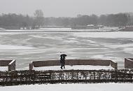 268_5042 An einem grauen Wintertag geht ein Paar am Stadtparksee spazieren - sie schützen sich mit einem Schirm gegen den Schneefall. Auf dem fast zugefrorenen See sitzen Möwen auf dem dünnen Eis. Im Hintergrund das Freibad Stadtparksee.