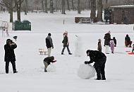 277_5017 Dichter Schnee fllt in Hamburg - im Becken des Planschbeckens, in dem im Sommer die Kinder im Wasser toben, baut ein Vater zusammen mit seinem Sohn einen groen Schneemann; die Mutter fotografiert die Aktion - andere Kinder spielen mit ihren Schlitten.