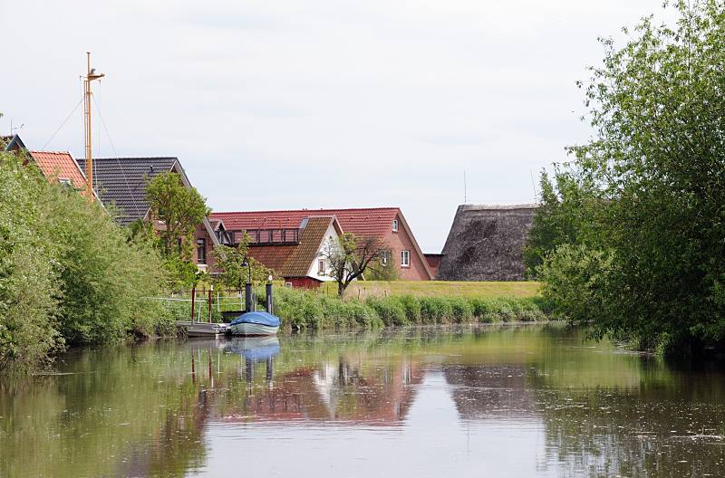 Bilder aus dem Alten Land, Wohnhäuser hinter dem Deich - Sportboot am Anleger. 049_7463 Die Wohnhäuser stehen vor Hochwasser geschützt hinter dem Deich der Este. Auf dem Fluss herrschte zu früheren Zeiten ein reger Güterverkehr, der mit Lastseglern ausgeführt wurde. Diese brachten die Waren an ihre Zielorte, wie z. B. die Obsternte auf die Hamburger Märkte. Jetzt ist der Lauf der Este ein reizvolles Sportbootrevier - die Fahrt entlang Obstbäumen und kleinen Ortschaften. Wo früher die Berufsschiffer ihre Kähne ankerten, befinden sich heute entlang des gesamten Verlaufs von Buxtehude bis Cranz zahlreiche Schlengel/ Liegeplätze für Segel- und Motorboote.