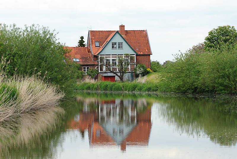 Bilder aus dem Alten Land - Lauf des Altländer Flusses Este. Wohnhaus am Esteufer - Weiden und Schilf, Spiegelung im Wasser. 050_4296 Wohngebäude direkt am Ufer der Este. Auf dem Fluss, der durchs Alte Land führt, herrschte zu früheren Zeiten reger Güterverkehr. Ewer mit flachem Boden und geringen Tiefgang brachten die Obsternte der Altländer Obstbauern auf die Hamburger Märkte. Jetzt ist der Lauf der Este für Sportboote ein reizvolles Wasserrevier in der Nähe Hamburgs.