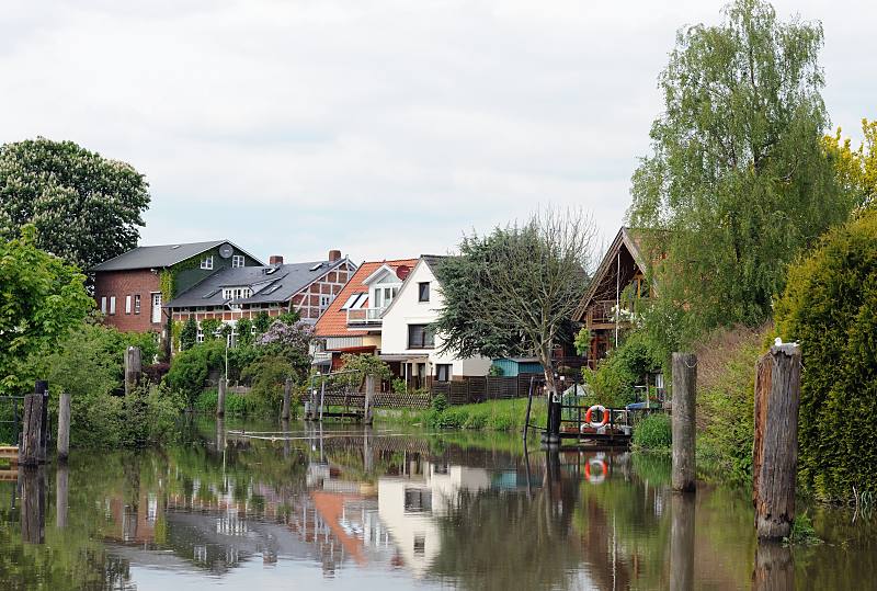 Bilder aus dem Alten Land - Wasserstrasse Este. Wohnhäuser am Ufer des Flusses - Bootsanleger und Holzdalben. 052_4318 Die Gärten und Wiesen der Wohnhäuser liegen direkt am Ufer der Este. Fast jedes Haus hat einen Bootsanleger für ein kleines Motorboot oder Segelschiff, um damit auf der Elbe zu segeln. Alte Holzdalben sind Zeugnis des früheren Güterverkehrs mit Lastseglern auf dem Fluss. Neben Erzeugnisse der Mühlen und Ziegeleien wurde auch die Obsternte auf dem Wasserwege transportiert.
