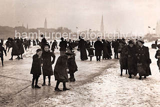 1086_3505_51 Kinder mit ihren Mttern auf dem Eis der zugefrorenen Aussenalster - einige haben Schlittschuhe untergeschnallt, andere glitschen auf dem Eis. Im Hintergrund Kirchtrme der Hansestadt Hamburg. 