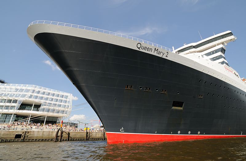 Schiffsbug der Queen Mary 2, Cruise Center + Hamburger Hafencity, Schaulustige am Kai  02_4353 Bug der Queen Mary 2 am Kreuzfahrtterminal im Hamburger Hafen. Schaulustige Hamburger stehen auf einer  Terrasse der Hafencity und bewundern das riesige Schiff.