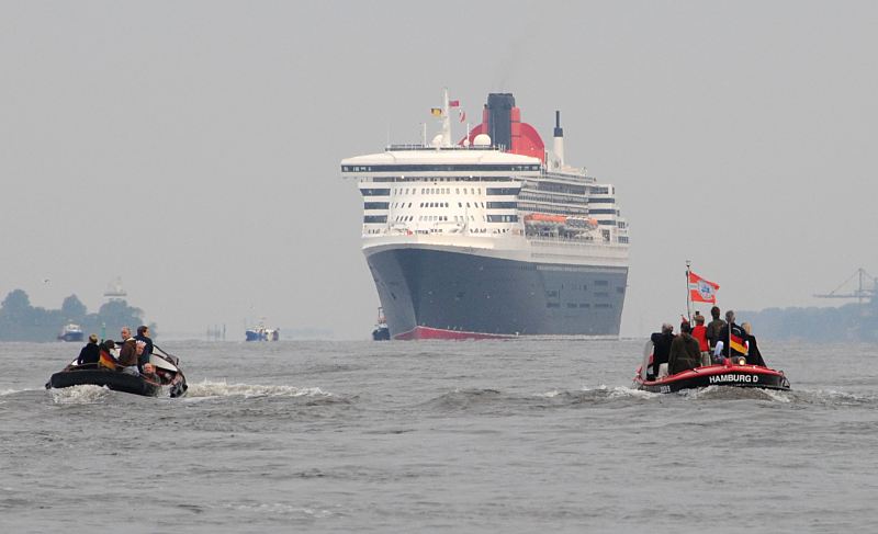 Kreuzfahrtschiff Queen Mary luft in Hamburg ein - historische Festmacherboote, Finkenwerder. 13_4638 Die Queen Mary 2 im Morgendunst vor Hamburg Finkenwerder. Zwei historische Festmacherboote aus dem Museumshafen Oevelgnne mit Schaulistigen Hamburgern an Bord fahren ihr entgegen, um das riesige Passagierschiff in Hamburg zu begrssen. www.fotograf-hamburg.de