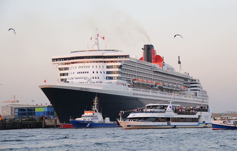 Schiffsfots aus Hamburg. Queen Mary 2 legt ab; Polizeiboot der Wasserschutzpolizei Hamburg sichert das Ablegemanver. Hamburger Hafenfotografie Christoph U. Bellin.  26_4917 Im Abendlicht legt die Queen Mary 2 Hamburger Kreuzfahrtterminal ab. Ein Polizeischiff am Bug des Passagierschiffs sichert das Manver und sperrt den Wasserraum ab, damit die Fahrgastschiffe und Privatboote das Ablegemanver nicht behindern.  www.fotograf- hamburg.de