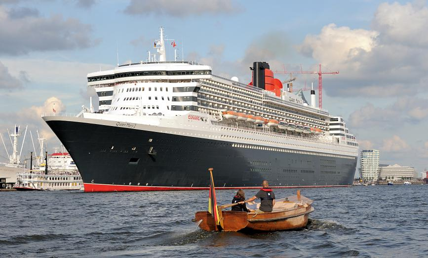 8560 Die Queen Mary 2 hat eine Lnge von 345m und eine Breite von 41m; das Passagierschiff hat eine Besatzung von 1253 und kann ca. 3000 Passagiere an Bord nehmen. Ein Holz-Tuckerboot mit Pinne fhrt dem Kreuzfahrtschiff entgegen.