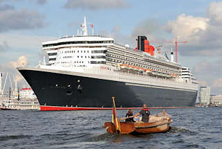 8560 Die Queen Mary 2 hat eine Lnge von 345m und eine Breite von 41m; das Passagierschiff hat eine Besatzung von 1253 und kann ca. 3000 Passagiere an Bord nehmen. Ein Holz-Tuckerboot mit Pinne fhrt dem Kreuzfahrtschiff entgegen.