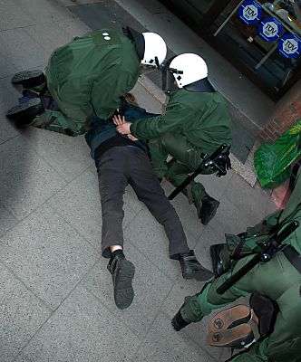 011_14244 - ein Demonstrant wird von Polizeikrften zu Boden gedrckt und die Hnde auf dem Rcken gefesselt; re. sind die Fsse eines weiteren zu erkennen, der sich in Polizeigewahrsam befindet.
